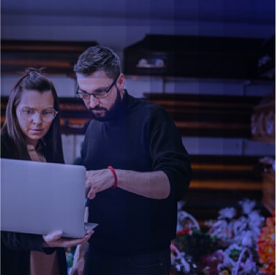 Funeral home staff using laptop technology in casket showroom.