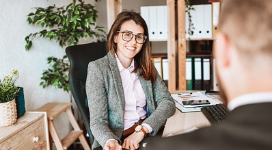 Professional woman in glasses smiling while meeting with a client in an office setting